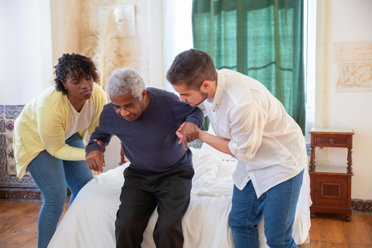 Caregivers helping an elderly man stand up